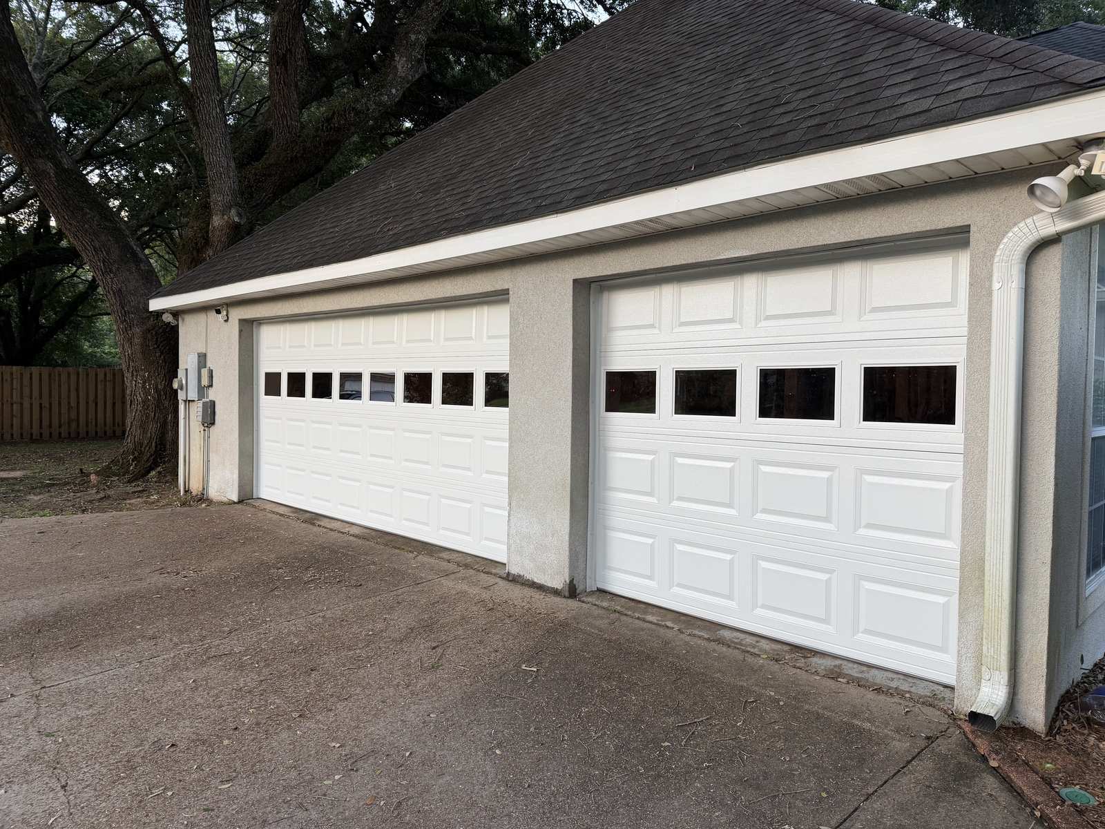 Stucco home with two newly installed white raised-panel sectional garage doors with window inserts